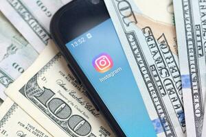 Smartphone screen with Instagram app and lot of hundred dollar bills. Business and social networking concept photo