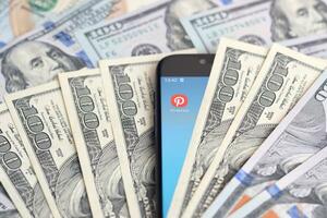 Smartphone screen with Pinterest app and lot of hundred dollar bills. Business and social networking concept photo