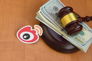 Weibo paper logo lies with judge gavel and hundred dollar bills. Entertainment lawsuit concept photo