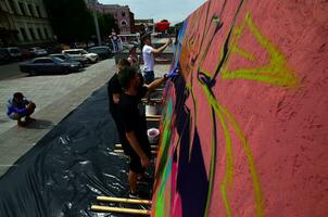 KHARKOV, UKRAINE - MAY 27, 2017 Festival of street arts. Young guys draw graffiti on portable wooden walls in the center of the city. The process of painting on walls with aerosol spray cans photo