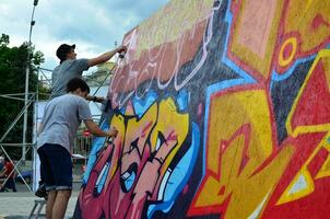 KHARKOV, UKRAINE - MAY 27, 2017 Festival of street arts. Young guys draw graffiti on portable wooden walls in the center of the city. The process of painting on walls with aerosol spray cans photo