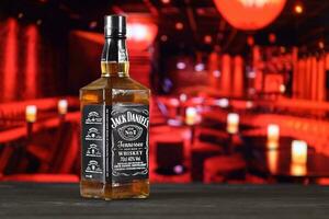 KHARKOV, UKRAINE - FEBRUARY 14, 2021 Jack Daniels No.7 whiskey bottle on wooden table with red bar interior on background. Elite alcohol photo