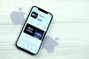 KHARKOV, UKRAINE - MARCH 5, 2021 Apple TV icon and application from App store on iPhone 12 pro display screen on white table photo