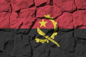 Angola flag depicted in paint colors on old stone wall closeup. Textured banner on rock wall background photo