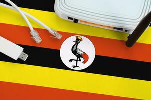 Uganda flag depicted on table with internet rj45 cable, wireless usb wifi adapter and router. Internet connection concept photo