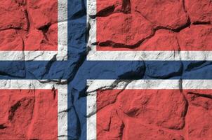 Norway flag depicted in paint colors on old stone wall closeup. Textured banner on rock wall background photo