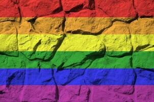 LGBT community flag depicted in paint colors on old stone wall closeup. Textured banner on rock wall background photo