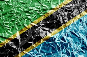 Tanzania flag depicted in paint colors on shiny crumpled aluminium foil closeup. Textured banner on rough background photo