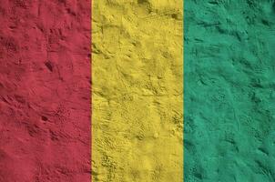 Guinea flag depicted in bright paint colors on old relief plastering wall. Textured banner on rough background photo