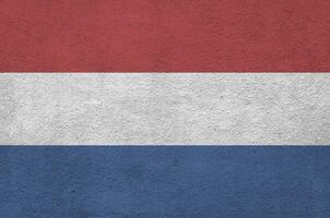 Netherlands flag depicted in bright paint colors on old relief plastering wall. Textured banner on rough background photo