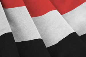 Yemen flag with big folds waving close up under the studio light indoors. The official symbols and colors in banner photo