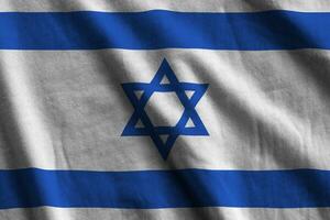 Israel flag with big folds waving close up under the studio light indoors. The official symbols and colors in banner photo