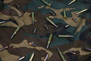 Many rifle bullets and cartridges on dark camouflage background photo