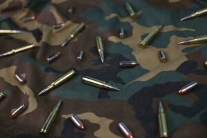 Many rifle bullets and cartridges on dark camouflage background photo