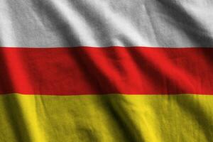 South Ossetia flag with big folds waving close up under the studio light indoors. The official symbols and colors in banner photo