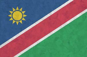 Namibia flag depicted in bright paint colors on old relief plastering wall. Textured banner on rough background photo