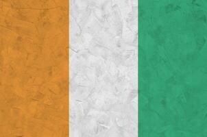 Ivory Coast flag depicted in bright paint colors on old relief plastering wall. Textured banner on rough background photo