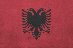 Albania flag depicted in bright paint colors on old relief plastering wall. Textured banner on rough background photo