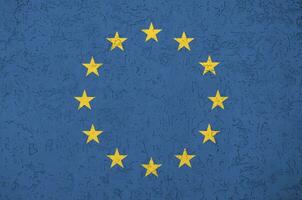 European union flag depicted in bright paint colors on old relief plastering wall. Textured banner on rough background photo