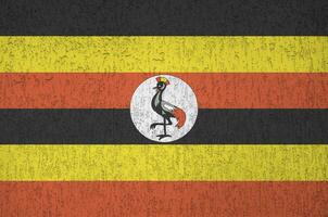 Uganda flag depicted in bright paint colors on old relief plastering wall. Textured banner on rough background photo