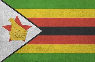 Zimbabwe flag depicted in bright paint colors on old relief plastering wall. Textured banner on rough background photo