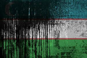 Uzbekistan flag depicted in paint colors on old and dirty oil barrel wall closeup. Textured banner on rough background photo