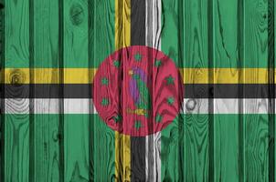 Dominica flag depicted in bright paint colors on old wooden wall. Textured banner on rough background photo