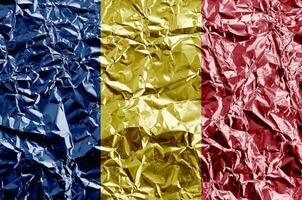 Romania flag depicted in paint colors on shiny crumpled aluminium foil closeup. Textured banner on rough background photo