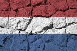 Netherlands flag depicted in paint colors on old stone wall closeup. Textured banner on rock wall background photo