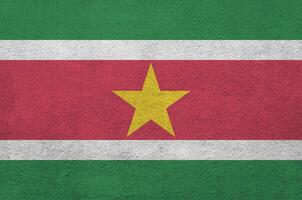 Suriname flag depicted in bright paint colors on old relief plastering wall. Textured banner on rough background photo