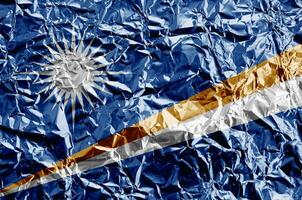 Marshall Islands flag depicted in paint colors on shiny crumpled aluminium foil closeup. Textured banner on rough background photo