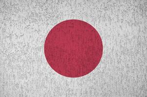 Japan flag depicted in bright paint colors on old relief plastering wall. Textured banner on rough background photo