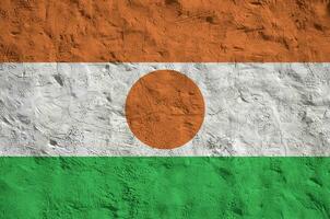 Niger flag depicted in bright paint colors on old relief plastering wall. Textured banner on rough background photo