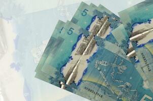 Los billetes de 5 dólares canadienses se encuentran apilados en el fondo de un gran billete semitransparente. presentación abstracta de la moneda nacional foto
