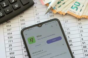 TERNOPIL, UKRAINE - AUGUST 3, 2023 Wise application on screen on modern smartphone and many bills of euro currency photo