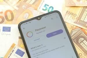 TERNOPIL, UKRAINE - AUGUST 3, 2023 Payoneer application on screen on modern smartphone and many bills of euro currency photo