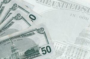 50 US dollars bills lies in stack on background of big semi-transparent banknote. Abstract business background photo