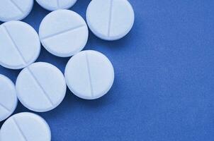 A few white tablets lie on a bright phantom classic blue color background surface. Background image on medical and pharmaceutical topics photo