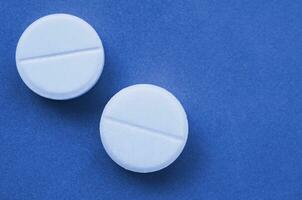 A few white tablets lie on a bright phantom classic blue color background surface. Background image on medical and pharmaceutical topics photo