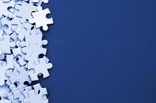 A pile of uncombed elements of a white jigsaw puzzle lies on the background of phantom classic blue color surface. Texture photo with copy space for text