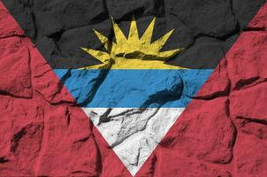 Antigua and Barbuda flag depicted in paint colors on old stone wall closeup. Textured banner on rock wall background photo