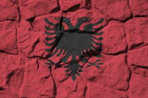 Albania flag depicted in paint colors on old stone wall closeup. Textured banner on rock wall background photo