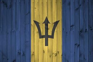 Barbados flag depicted in bright paint colors on old wooden wall. Textured banner on rough background photo