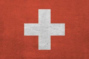 Switzerland flag depicted in bright paint colors on old relief plastering wall. Textured banner on rough background photo