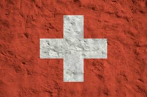 Switzerland flag depicted in bright paint colors on old relief plastering wall. Textured banner on rough background photo