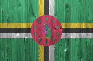 Dominica flag depicted in bright paint colors on old wooden wall. Textured banner on rough background photo