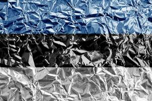 Estonia flag depicted in paint colors on shiny crumpled aluminium foil closeup. Textured banner on rough background photo