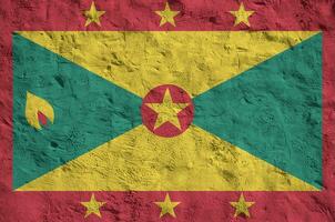 Grenada flag depicted in bright paint colors on old relief plastering wall. Textured banner on rough background photo