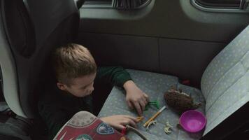 A boy sitting on a cars floor playing with some toys on a back seat video