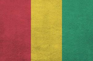 Guinea flag depicted in bright paint colors on old relief plastering wall. Textured banner on rough background photo